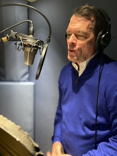 A man in blue shirt and headphones near microphone.